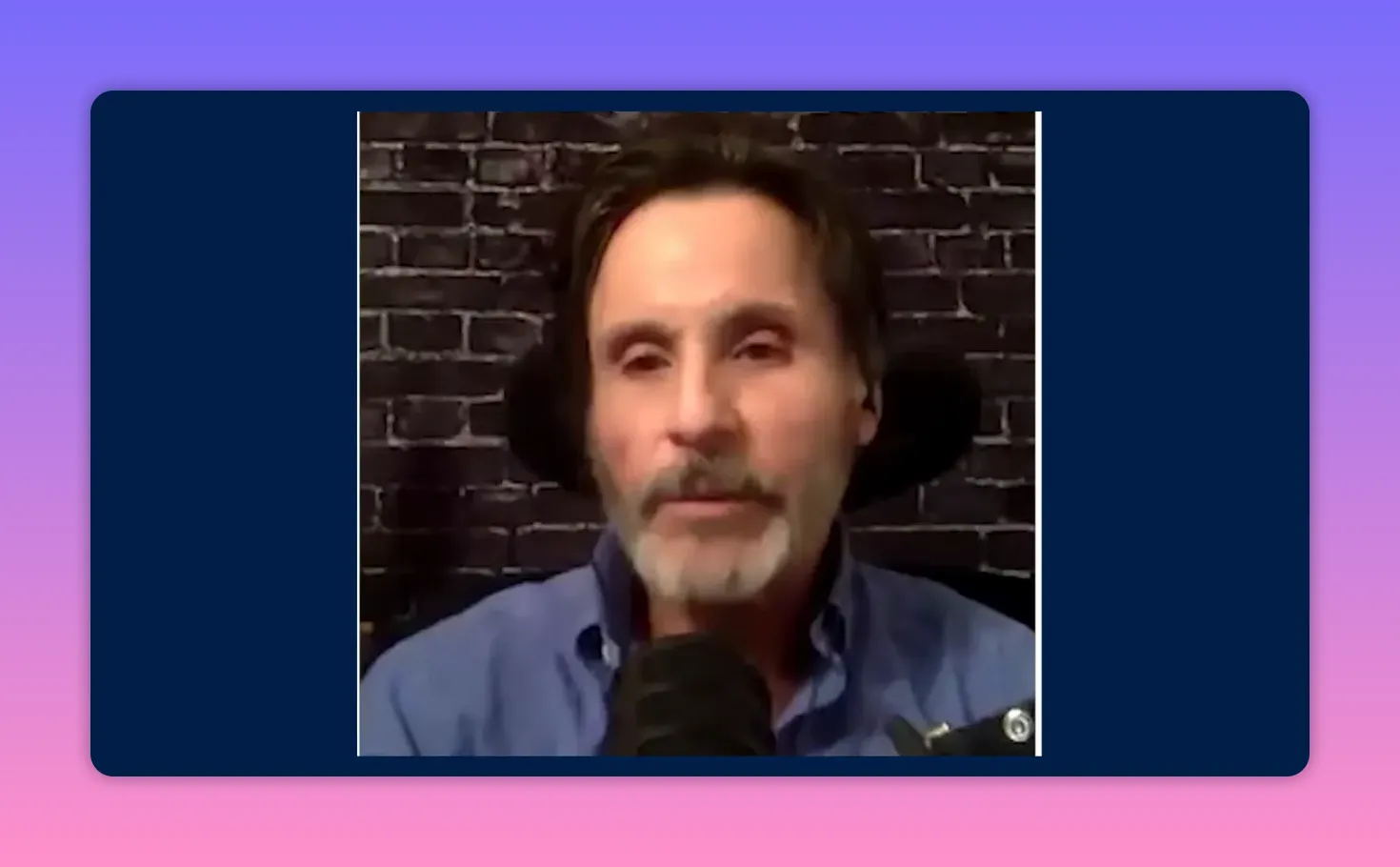 Well-centered clear shot of a podcast speaker at a microphone against a brick-wall background.